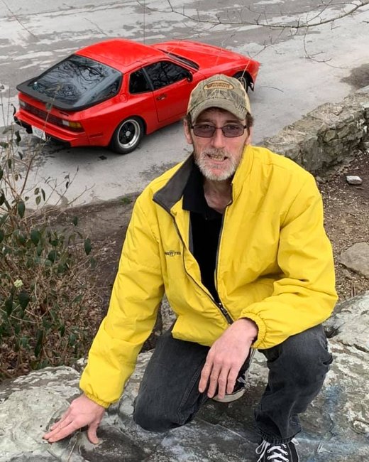 Sig crouching on rocks above a red car.